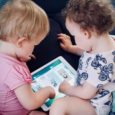 two toddlers both sitting with a tablet between them 